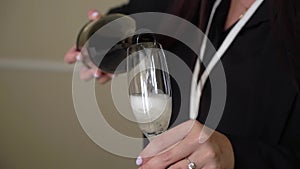 Woman pours champagne to glass. Waiter fill with alcoholic drinks in restaurant.
