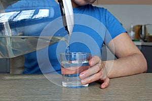 Woman pours clean water from a glass teapot into a glass beaker