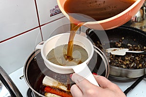 The woman pours the decoction of the mushroom soup through a plastic strainer.