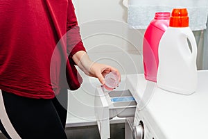 A woman pours detergent into the washing machine tray.