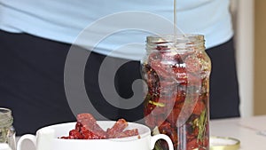 A woman pours olive oil over sun-dried tomatoes in a jar. Cooking at home. Close-up shot