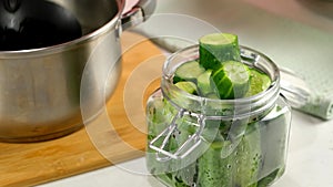 Woman pours saline to cucumbers in glass jar to cook pickles on kitchen at home.