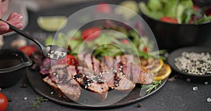 Woman pours sesame seeds onto Sliced Fried grilled piece of Organic Tuna Steak on a black ceramic plate with salad