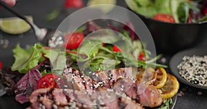 Woman pours sesame seeds onto Sliced Fried grilled piece of Organic Tuna Steak on a black ceramic plate with salad