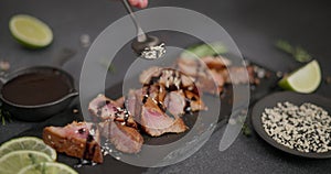 Woman pours sesame seeds onto Sliced Fried grilled piece of Organic Tuna Steak on a black stone serving board