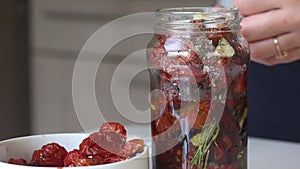 A woman pours spices and sun-dried tomatoes into a jar with olive oil. Cooking sun-dried tomatoes in olive oil. Close-up shot_