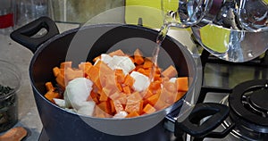 A woman pours water into a pan with ingredients standing on a gas stove for making cream soup. Healthy eating concept