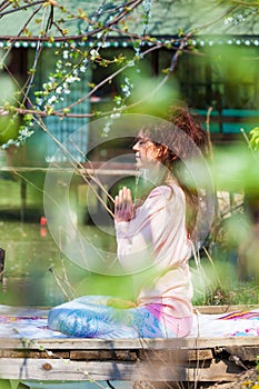 Woman practice yoga outdoor spring summer  day by the lake sit in lotus position with hands in anjali mudra