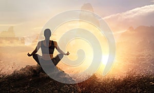 Woman practices meditating yoga at is an asana on a stone, sunset mountains background