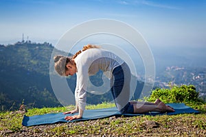 Woman practices yoga asana Marjariasana outdoors