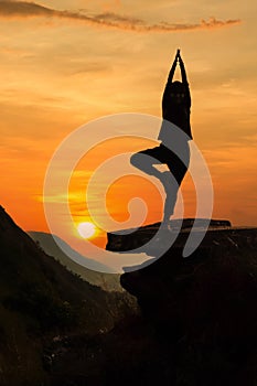 Woman practices yoga on a background of sunset and mountains. Woman doing yoga on stone in the mountains. Young Caucasian woman do