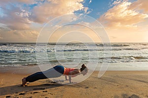 Woman practices yoga at the beach on sunset
