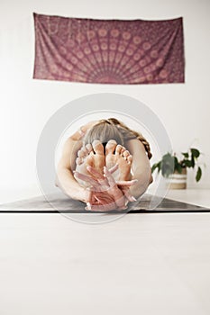A woman practices yoga, she is bent on the floor holding her feet with her hands in gyan mudra