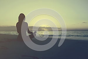 Woman practices yoga meditation lotus pose beach sunrise