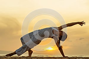 Woman practices yoga at the seashore at sunset on Bali in indonesia
