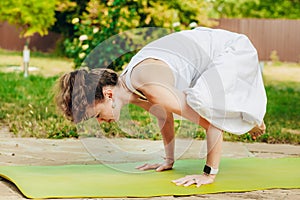 Woman practices yoga in summer garden: Kakasana, Crow Pose, with bent arms