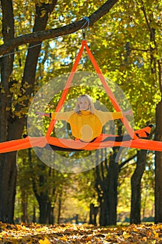 Woman practicing aerial silks on a trees background in autumn