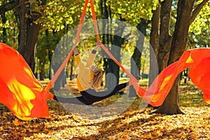 Woman practicing aerial silks on a trees background in autumn