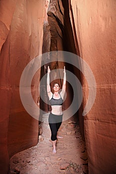 Woman practicing exalted warrior yoga pose in red rock slot canyon