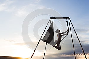 Woman practicing fly dance yoga poses in hammock outdoors at sunset