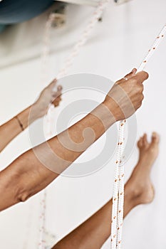 Woman practicing iyengar yoga using wall ropes in studio, padangusthasana