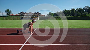 Woman practicing sprinter position on racetrack.