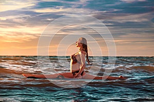 Woman practicing SUP yoga at sunset, meditating on a paddle board. photo