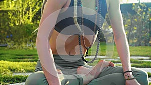 Woman is practicing Uddiyana Bandha technique sitting on the lawn in lotus pose