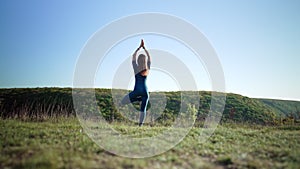 Woman practicing in Vriksasana - pose of tree, doing yoga on high hill. Meditation. Flexibility workout at nature