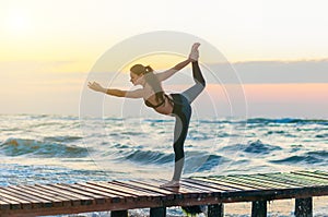 Woman practicing Warrior yoga pose outdoors over sunset sky background