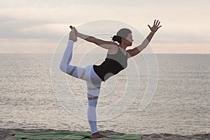 Woman practicing yoga on the beach. King Dancer Pose, Natarajasana. Outdoors sports. Healthy living.