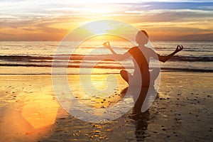 Woman practicing yoga on the beach in the glow of an amazing sunset.