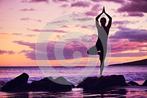 Woman practicing yoga on the beach at sunset