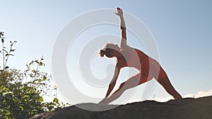 Woman is practicing yoga at a beautiful green place on the top of a mountain in slow motion