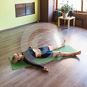 Woman practicing yoga, doing shavasana exercise with pranayama breathing practice, relaxing asana, lying on a mat in the room