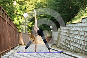 A woman practicing yoga, doing a twisting exercise Parivritta Padottanasana, exercising on a summer morning in the park