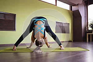 A woman practicing yoga doing a variation of the prasarita padottanasana exercise, leaning forward with her legs apart