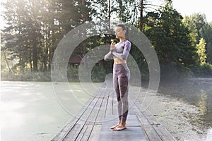 A woman practicing yoga, doing a variation of the vrikshasana exercise, tree pose with namaste