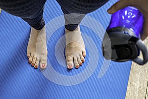 Woman practicing yoga, holding a bottle water. Feet with pink pedicure of woman on blue mat