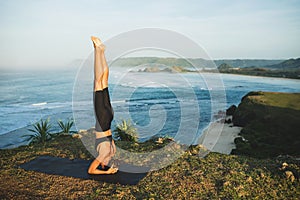 Woman practicing yoga and making handstand pose outdoor with amazing ocean view