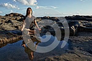 Woman practicing yoga and meditation in lotus position on black stones near the sea