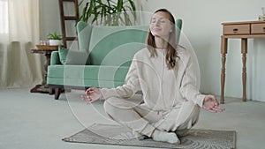 A woman practicing yoga and meditation in the lotus position sitting on the floor of at home