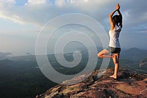 Woman practicing yoga at mountain peak cliff edge