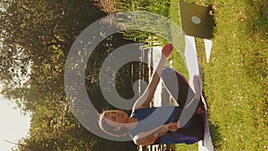 Woman practicing yoga on nature with laptop, doing online lessons.Vertical video