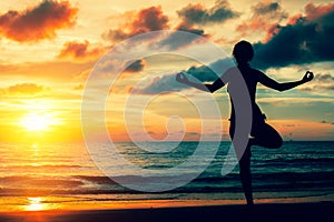 Woman practicing yoga on the ocean coast during a magical sunset. Silhouette.