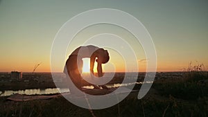 Woman practicing yoga in the park at sunset