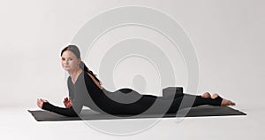 A woman practicing yoga, performing the Bhekasana exercise, frog pose, training in a black one-piece sports overalls on a mat