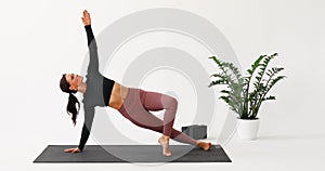 Woman practicing yoga, performing Vasishthasana exercise, side plank with arm raised up, training in sportswear in a bright room