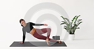 A woman practicing yoga performs a variation of Vasishthasana exercise, dynamic side plank, training in sportswear in a room