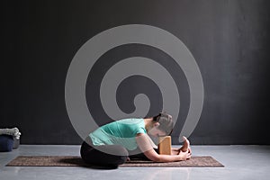 Woman practicing yoga, Seated forward bend pose , using brick or block